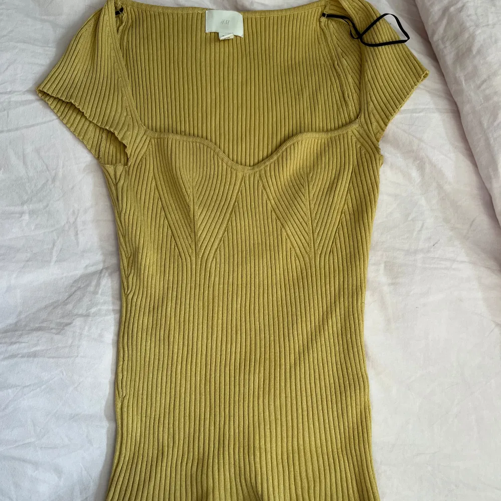 Säljer en snygg gul ribbad topp från H&M med korta ärmar och en smickrande passform. Toppen har en fyrkantig halsringning och är perfekt för både vardag och speciella tillfällen. Passar utmärkt till jeans eller kjol. 🌟. Yläosat.