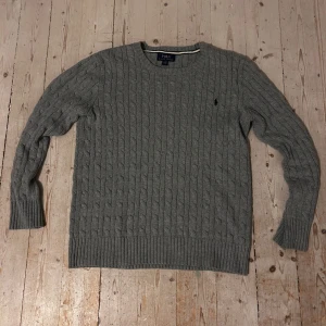 Grå stickad tröja från Ralph Lauren - Säljer en stilren grå stickad tröja från Ralph Lauren med kabelstickat mönster. Tröjan är i storlek  XL 18-20 i barn storlek men motsvarar som storlek S i herr storlek. Tröjan är i fint skick. Skriv om du har några frågor🤩