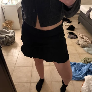 Svart kortkjol med volang - Snygg svart kortkjol med volangdetaljer. Perfekt för en stilren look. Kjolen har en elastisk midja för bekväm passform.