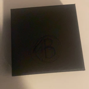 Svart armband med kedjedetalj - Snyggt svart armband med en elegant kedjedetalj. Perfekt för att ge en stilren touch till din outfit. Armbandet har en diskret logga och ett smidigt lås.