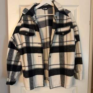Snygg rutig overshirt i svart och vit med knappar framtill. Perfekt för lager-på-lager-stil. Två bröstfickor med knappar ger en cool look.