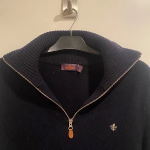 Mörkblå halfzip från Morris - Säljer en stilren mörkblå tröja från Morris med dragkedja och ribbad krage. Tröjan har en liten broderad detalj på bröstet och långa ärmar. Perfekt för kyligare dagar. Riktigt skön och i 100% merinoull. Storlek M men kan passa L också