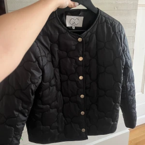 Svart quiltad jacka  - Snygg svart quiltad jacka med rund hals och knappar framtill. Perfekt för en stilren look.