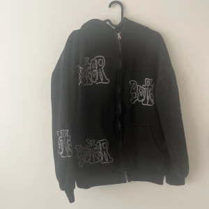 Svart hoodie från Butter - Säljer en svart hoodie från Butter med coola vita tryck över hela tröjan. Den har en dragkedja framtill och en skön huva. Perfekt för en avslappnad stil.
