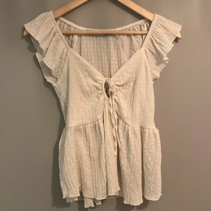 Vit blus med volangdetaljer från 157 - Säljer en söt vit blus från 157 med volangdetaljer och knytning framtill. Blusen har en luftig passform och korta ärmar, perfekt för varma dagar. Den är gjord i ett lätt och bekvämt material. Använd några gånger bara💕