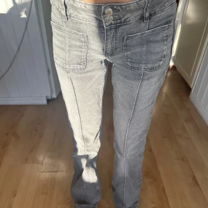 Grå jeansbyxor med fickor - Snygga grå jeansbyxor med framträdande fickor framtill och en klassisk knappstängning. Byxorna har en rak passform och är perfekta för en avslappnad stil. De är tillverkade i ett bekvämt material som ger en skön känsla hela dagen. 