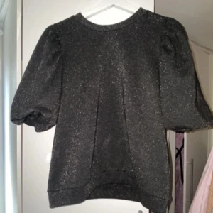 Svart glittrig tröja från Kappahl - Säljer en svart glittrig tröja från Kappahl med puffiga ärmar. Perfekt för att lägga till lite glitter i vardagen. Tröjan har en rund hals och är i en bekväm passform.  .Den var tänkt till nyår. Hann aldrig använda den så säljer den. Köpt för typ 150-200              