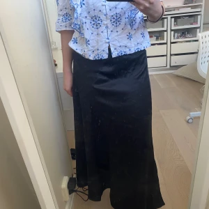 Svart långkjol i satin - Elegant svart långkjol i satin som ger en lyxig känsla. Perfekt för att skapa en stilren look. Kjolen har en slät yta och faller vackert längs benen med en slits. Kontakta för fler bilder☺️☺️