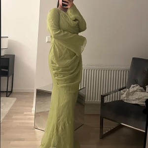 Limegrön långklänning - Säljer en elegant limegrön långklänning med långa ärmar och en draperad design. Perfekt för en somrig look eller speciella tillfällen. Klänningen har en lös passform och är tillverkad i ett lätt material som ger en luftig känsla.