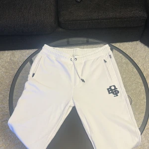 Vita mjukisbyxor från Boss storlek L, Äkta - Snygga vita mjukisbyxor från Boss med elastisk midja och snörning. Byxorna har praktiska fickor med dragkedja och en stilren logga på benet. Perfekta för en avslappnad stil. Använda 1-2 gånger
