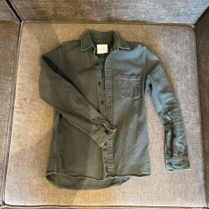 Grön skjorta från A Day's March - Snygg grön skjorta från A Day's March med en bröstficka och knappar framtill. Perfekt för en stilren look. Skjortan har långa ärmar och en klassisk krage.