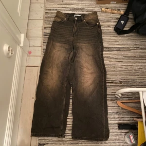 bershka jeans - Säljer ett par bruna jeansbyxor med hög midja och vida ben. Byxorna har en klassisk femficksdesign och en lätt tvättad look. Perfekta för en avslappnad stil.
