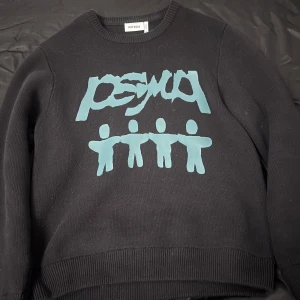 Svart Weekday tröja - Snygg svart tröja från Weekday med ett unikt turkost tryck på framsidan. Tröjan har en rund halsringning och ribbade muddar vid ärmslut och nederkant. Perfekt för en avslappnad stil.