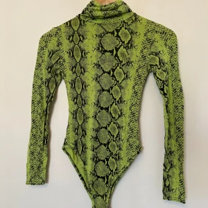 Grön ormmönstrad bodysuit från Boohoo - Säljer en cool grön bodysuit med ormmönster från Boohoo. Den har en polokrage och långa ärmar.