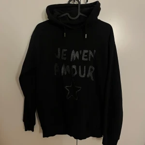 Svart hoodie från Gina Tricot - Säljer en svart hoodie från Gina Tricot med text och en stjärna i glittrigt material på framsidan. Tröjan har långa ärmar och en klassisk huva med dragsko. Perfekt för en avslappnad stil.