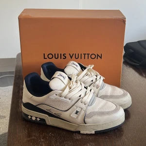  Louis Vuitton trainers  - Snygga vita sneakers från Louis Vuitton med marinblå detaljer och snörning. Skorna har en unik design med märkets logga på sulan och #54 på hälen. Kan inte äkthetsverifiera dem. Passar 45 bättre än 46.storlek 46. Fint skick, box, skor och dustbags medföljer. 
