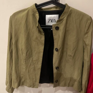 Olivgrön jacka från Zara - Snygg olivgrön jacka från Zara med knappar framtill. Den har en stilren design med en kortare passform och långa ärmar. Perfekt för att ge en elegant touch till din outfit. Endast använd en gång.