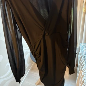Svart klänning från Nelly - Snygg svart klänning från Nelly med långa transparenta ärmar och omlott-design.  Använd cirka 3 gånger. Fler bilder kan skickas privat.