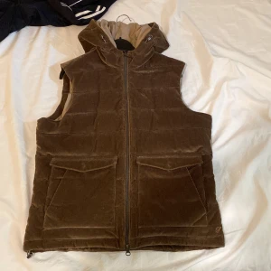 Brun manchester väst från Stenströms - En brun manchester väst från Stenströms med dragkedja och huva. Västen har två stora fickor framtill och är quiltad för extra värme. Kan gärna byta mot en parfym eller annat kul 