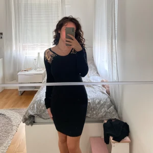 Kort elegant klänning med gulddetaljer. - Säljer min jättesköna svarta klänning med guldiga paljetter vid axlarna. Ganska varmt och tjockt material, passar till hösten. Köpt i USA och Använt en gång länge sen. Säljer för 169 kr. 