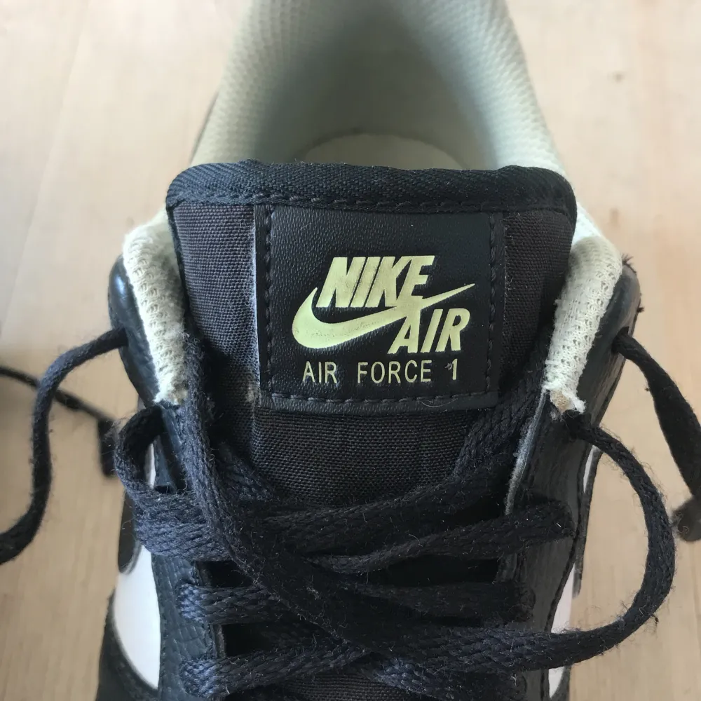 Ett par Nike Air Force 1 sneakers i svart, vit  och ljusgul färg. Skorna har snörning och en perforerad tåbox för ventilation. De är i storlek EUR 40, 25.5 cm. Skor.