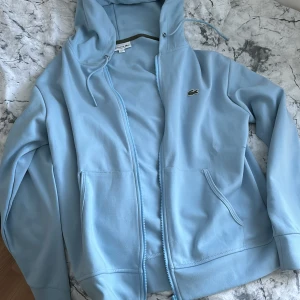 Ljusblå Lacoste zip - Den är helt oanvänd. Nypris ca 1800, slutsåld på många sidor.