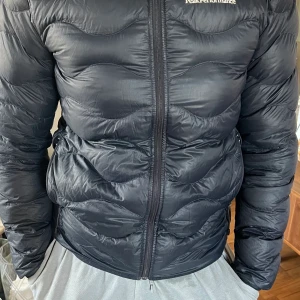 Peak Performence  - Marinblå dunjacka, använd och kan behöva puffas. Trasig dragkedja och ett litet hål i fickan, se bild 3