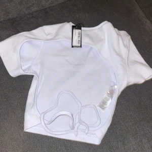 Vit topp med öppenrygg  - Supersnygg vit topp med öppenrygg, öppningen är väldigt snyggt asymmetrisk med snören längst ned. Helt oanvänd, lappen kvar. Storlek 38