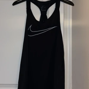 Svart Nike träningslinne - Svart Nike träningslinne med halvt öppen rygg med bara två tjockare band. Väldigt tunn och skön att träna i nu på sommaren. Använt 1-2 gånger så bra skick!