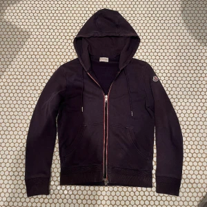 Moncler ”Maglia Cardigan” - Skit snygg zip-hoodie från Moncler! Tröjan är äkta, 7/10 skick (dragkedjan är skadad samt små defekter på armen). Storleken är S men passar också XS. Fråga gärna om bilder på taggen eller annat!