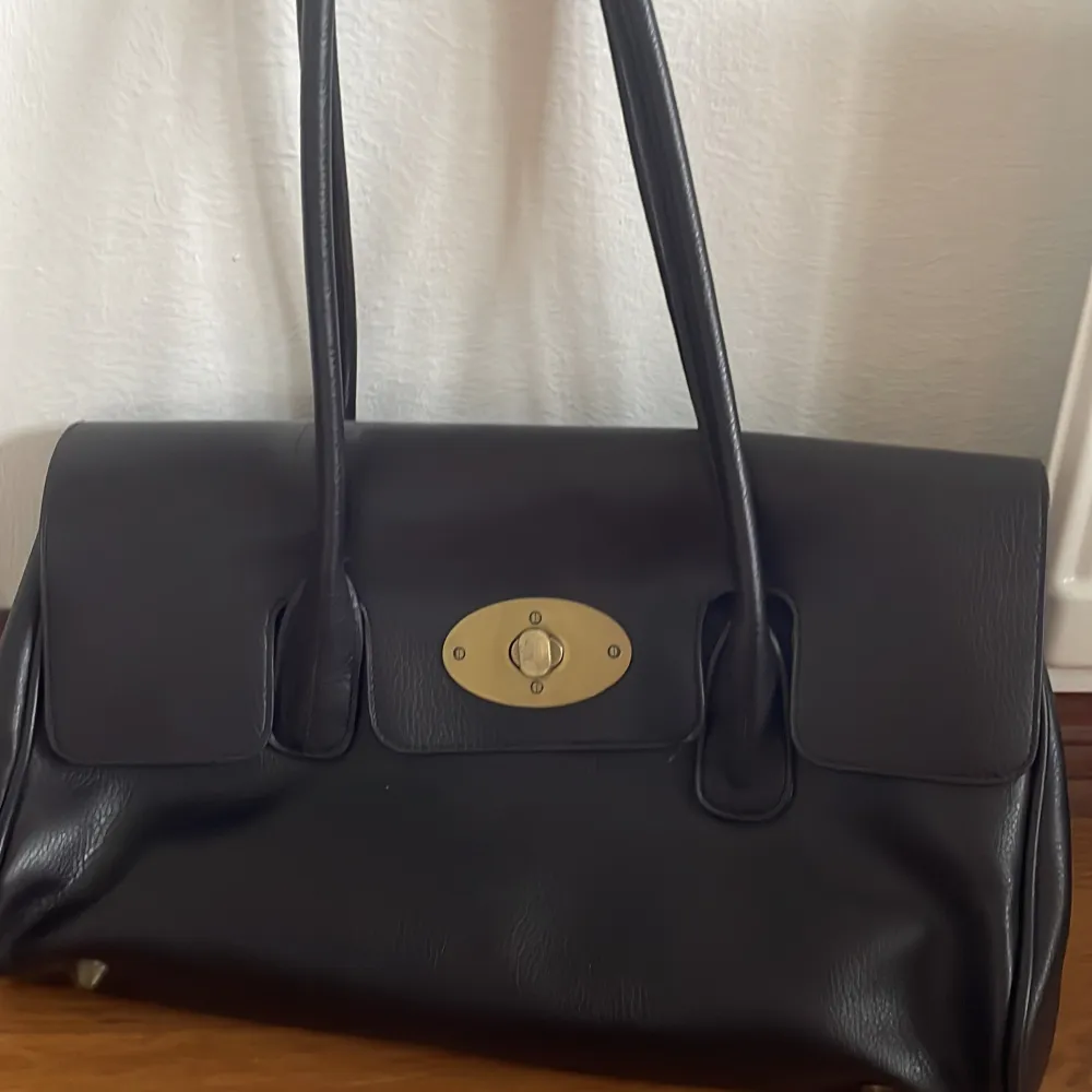 En mörkbrun handväska med guld detaljer. Jättefin men kommer inte till användnings. Väskor.