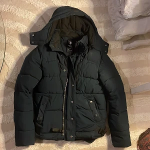 Varm Jacka från Smog - En mörkblå/svart skön varm jacka från märket SMOG, det finns även pälskrage som kommer med som man sätter fast i huvan. Finns i storlek S! Jag är tjej och hade den mycket under vintern, den håller värmen jättebra och kan dras upp ända till ansiktet.