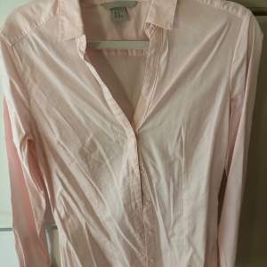 Elegant skjorta som sitter smickrande på kroppen- ursäkta att den lite skrynklig.  Den är ljus rosa i färgen Storlek M/L.  Nytt och oanvänd