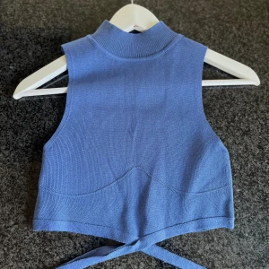 Blå topp med korsband - En blå kortare topp med band som korsar runt midjan.  Storleken är EUR 38