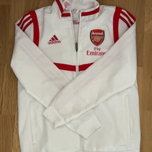 Arsenal traksuit tröja - Säljes pga att jag växte ut den får något år sedan och den kommer aldrig till användning. Den är inte gjort av samma material som dem kända psg tröjorna men är ändå väldigt bra kvalitet. Den är även i väldigt bra skick.