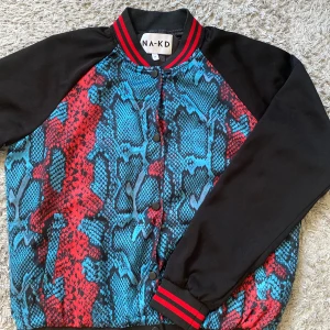 Bomberjacka  - Cool röd/blå/svart mönstrad bomberjacka från NA-KD som aldrig är använd.