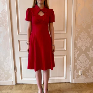 Röd klänning, hög krage, Emmy design - Röd klänning i bekvämt material. Storlek 38. Hög krage och puffiga ärmar. Modellen på bilden är 173 cm och har storlek 38 i de flesta andra kläder. Aldrig använd. Vi har lagt ner vår klänningsbutik och säljer ut. Ny pris är 2000-3000kr