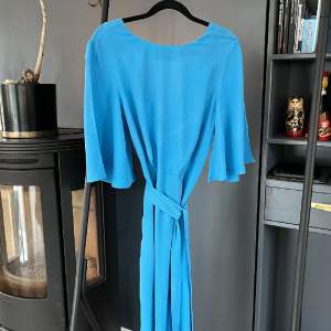 En fantastiskt fin blå klänning från H&Ms tidigare premiumkoncept. V-ringad rygg, vida ärmar och band som går att vira två varv runt midjan om man vill. 100% viskos. Storlek 36. Rökfritt hem, dock ej djurfritt.