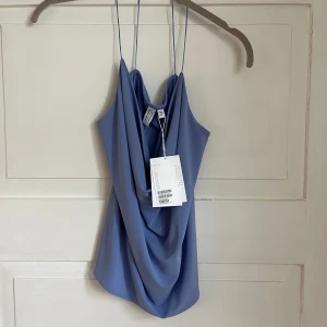 Topp från Andotherstories - Helt oanvänd ljusblå/lila topp med kriss-kross band i ryggen från Andotherstories, strl 38. 100kr