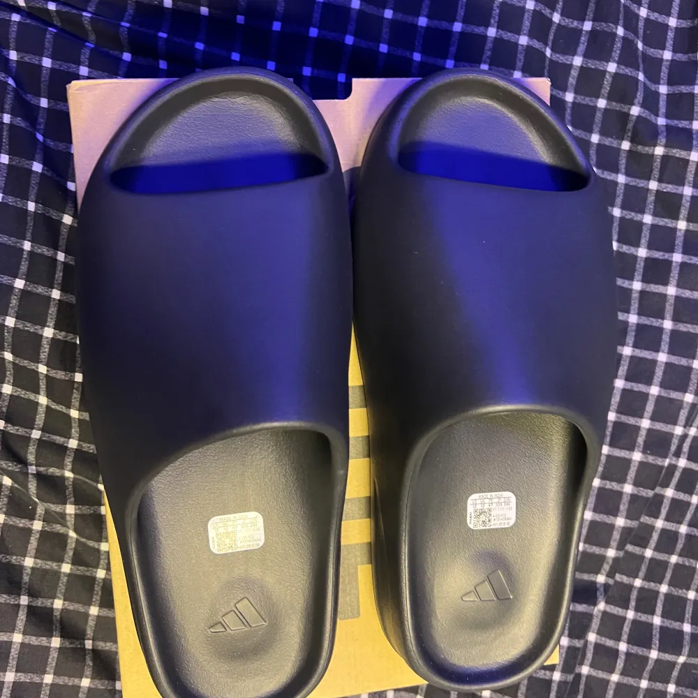 Säljer ett par yeezy slides i colorwayen Dark Onyx. De är i storlek 47 men är små i storleken så de passar 46 också. De är helt nya deadstock och aldrig använda, tog de bara ut ur lådan för att ta bilderna. Pris kan diskuteras.. Skor.