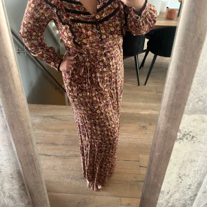 Mönstrad klänning med blommor  - Mönstrad klänning med blommor, liten defekt på bandet man knyter runt. Använd fåtal gånger. Nypris 1800 kr. 