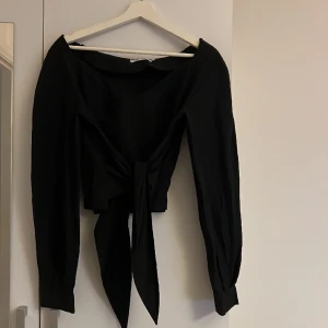 Svart topp  - Svart långärmad topp i kavajliknande material. Knytning i midjan och en liten dragkedja i ena sidan. Ganska liten i storleken 
