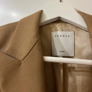 Sandro Kavaj - Superfin kavaj från Sandro Paris i fint skick. Köpt på NK i Stockholm för 2 år sedan, och är mycket sparsamt använd sen dess. Fin kamelbrun färg med guldigt foder. Perfekta vårjackan!