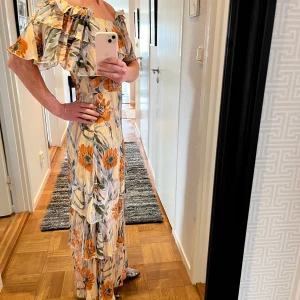 Långklänning från Valerie - Långklänning från Valerie i stl 38. Använd endast en gång. Nyskick. Går till anklarna för den som är 170 cm lång. Härligt material, volang, fint blommönster. Stl 38 men kan funka på den som är 36 i stl. 