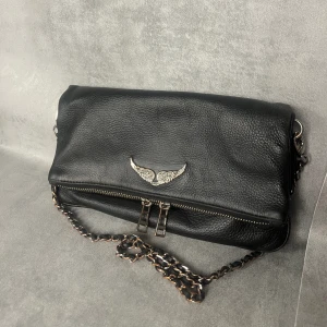 Zadig & Voltaire Rock Clutch - Väskmått: 27 x 13 x 2cm Kedjemått: 33 & 57cm  Kedja och magnetlås Detaljer: varumärkets märke med stenar 3 fak, varav ett med inneficka. Väska i relativt bra skick, 33cm kedja välanvänd, 57cm kedja helt oanvänd. Går att ta bort band 