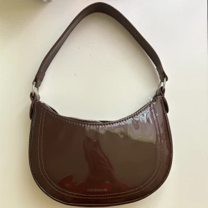 Brun handväska🌸 - En brun glansig hand väska. Säljer då den inte kommer till användning längre. Finns även ett längre . Använd några gånger men inga defekter🌸