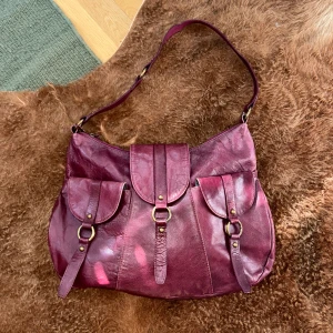 Vinröd axelväska - En otrolig everyday-väska med många fack. Rymmer anteckningsblock och en mindre dator. Detaljer i mässing och i äkta läder