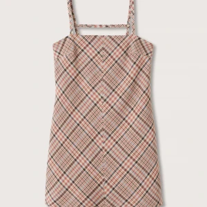 Miniklänning med smala axelband  - Rutig klänning med tunna axelband och dragkedja i ryggen. Köpt från Mango. Mycket skönt material med 60 % viskos, 38 % polyester och 2 % elastan. Innerklänning/foder i 100 % polyester. Aldrig använd!