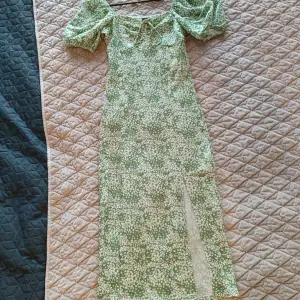 Lång grön klänning i storlek xs från Gina Tricot! Klänningen är grön och vit i blommigt mönster med slits vid ena sidan av benen och knytning vid bröstkorgen. Klänningen är puffärmad och figursydd vilket ger en fin siluett! Klänning är helt oanvänd! 