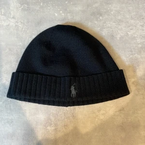 Ralph lauren mössa - En svart  Ralph lauren mössa med ett gråt märke. i nyskick köpte den för två år sedan men aldrig använd  skick är 10/10🤩 den är ganska sällsynt eftersom man inte kan köpa den längre😃 ny pris var runt 600kr